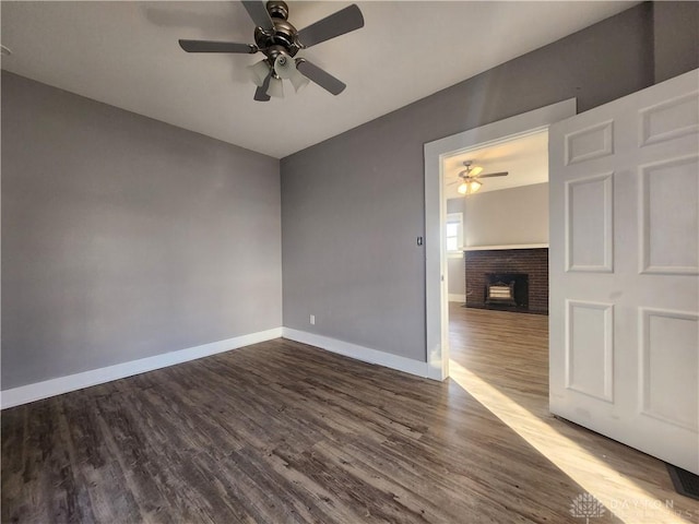 spare room featuring ceiling fan, wood-type flooring, and a brick fireplace