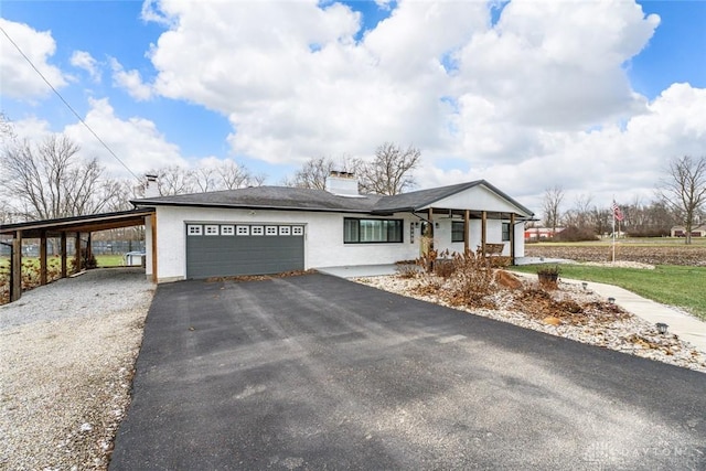 ranch-style home featuring a porch, aphalt driveway, an attached garage, an attached carport, and a chimney