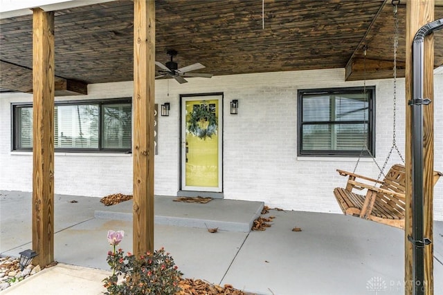 entrance to property with ceiling fan, brick siding, and covered porch