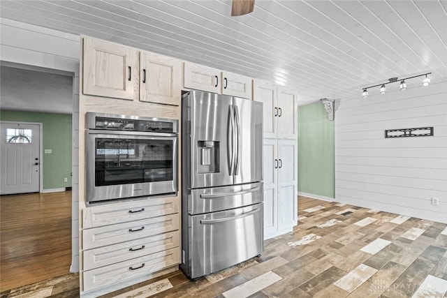 kitchen featuring wood walls, track lighting, appliances with stainless steel finishes, and wood finished floors