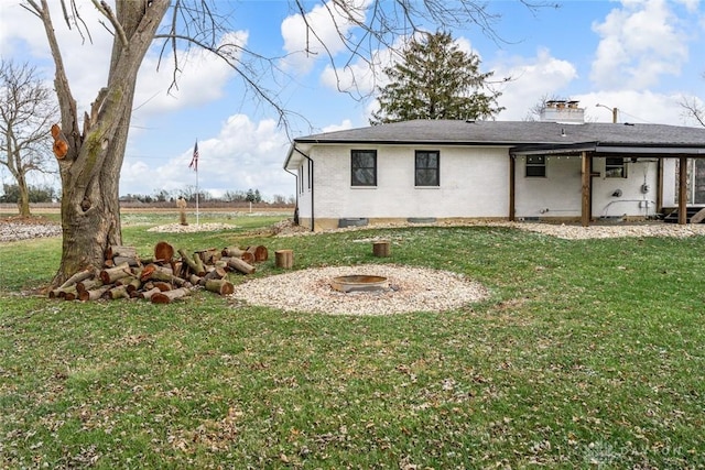 rear view of house with an outdoor fire pit, a chimney, a lawn, and brick siding