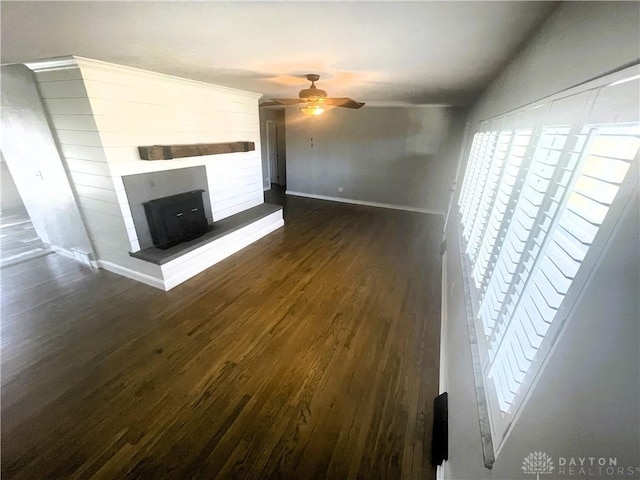 unfurnished living room featuring dark wood-style floors, a fireplace with raised hearth, ceiling fan, and baseboards