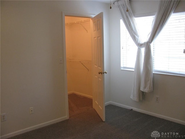 unfurnished bedroom with dark colored carpet, a spacious closet, and a closet