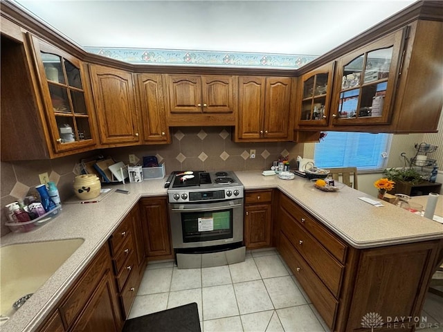 kitchen featuring decorative backsplash, stainless steel range oven, light tile patterned floors, and sink