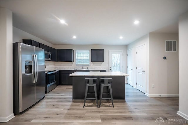 kitchen featuring a kitchen bar, appliances with stainless steel finishes, light wood-type flooring, sink, and a kitchen island