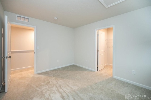 unfurnished bedroom featuring a spacious closet, a closet, and light colored carpet