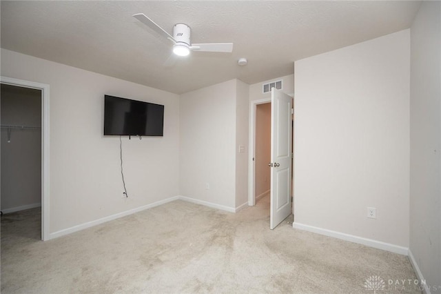 unfurnished bedroom featuring light carpet, a closet, a spacious closet, and ceiling fan