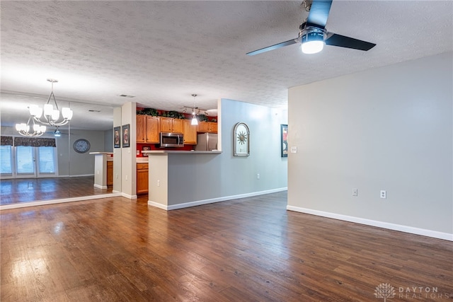 unfurnished living room with ceiling fan with notable chandelier, a textured ceiling, and dark hardwood / wood-style flooring