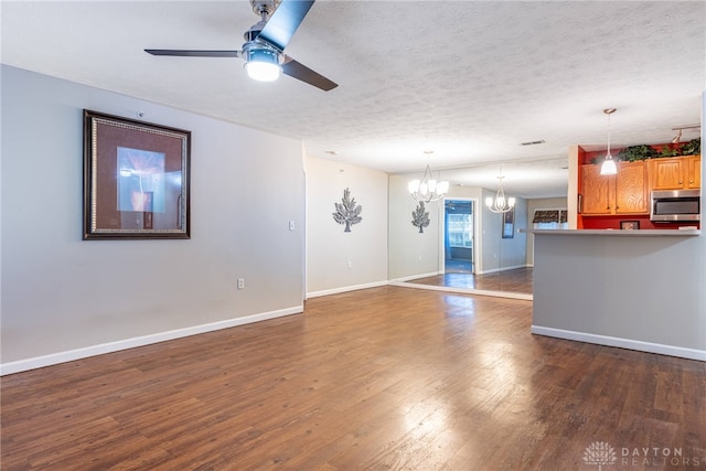 unfurnished living room with ceiling fan with notable chandelier, dark hardwood / wood-style flooring, and a textured ceiling