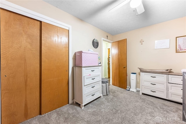 bedroom featuring a textured ceiling, light colored carpet, a closet, and ceiling fan