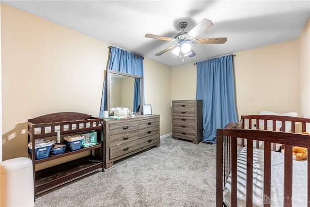 bedroom with a textured ceiling, ceiling fan, carpet, and a crib