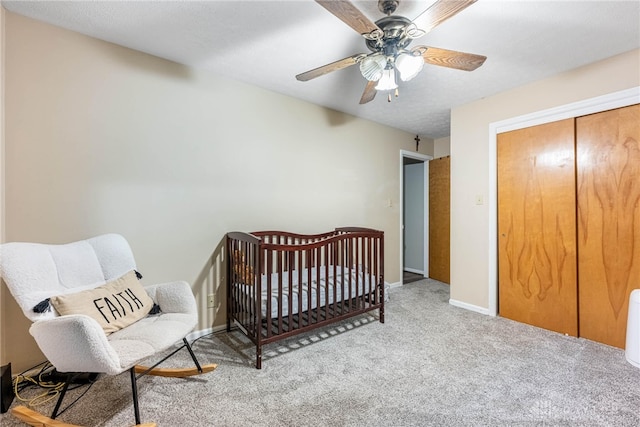 bedroom with light carpet, a textured ceiling, ceiling fan, a nursery area, and a closet