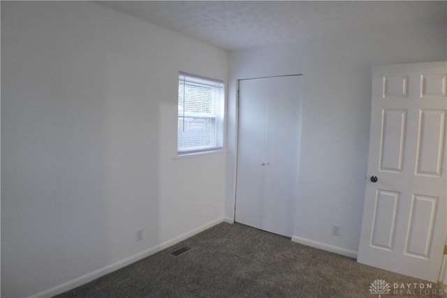 unfurnished bedroom with dark colored carpet and a closet