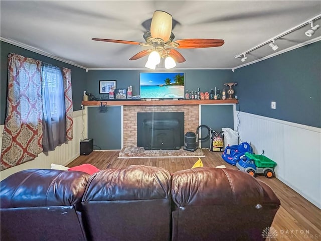 living room with a wood stove, ceiling fan, rail lighting, wood-type flooring, and ornamental molding