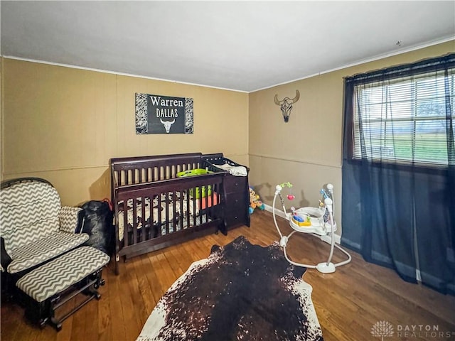 bedroom featuring wood-type flooring, a nursery area, and ornamental molding