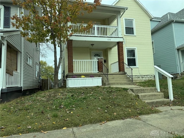 view of front of house with covered porch, a balcony, and a front yard