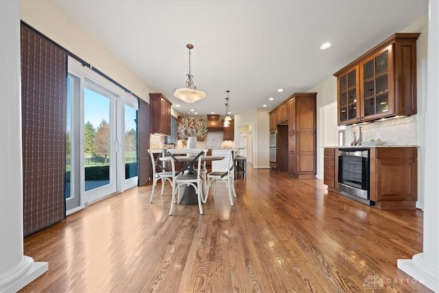 dining room featuring wood-type flooring, beverage cooler, and ornate columns