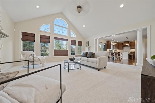 living room with ornate columns, ceiling fan, high vaulted ceiling, and light colored carpet