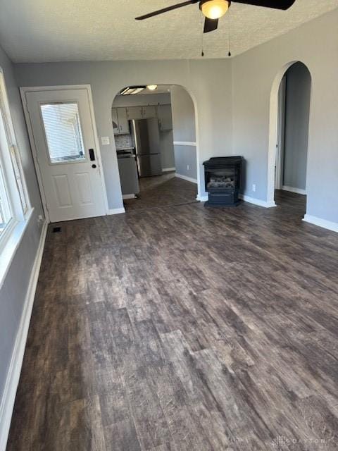 unfurnished living room with a textured ceiling, a wood stove, ceiling fan, and dark hardwood / wood-style floors