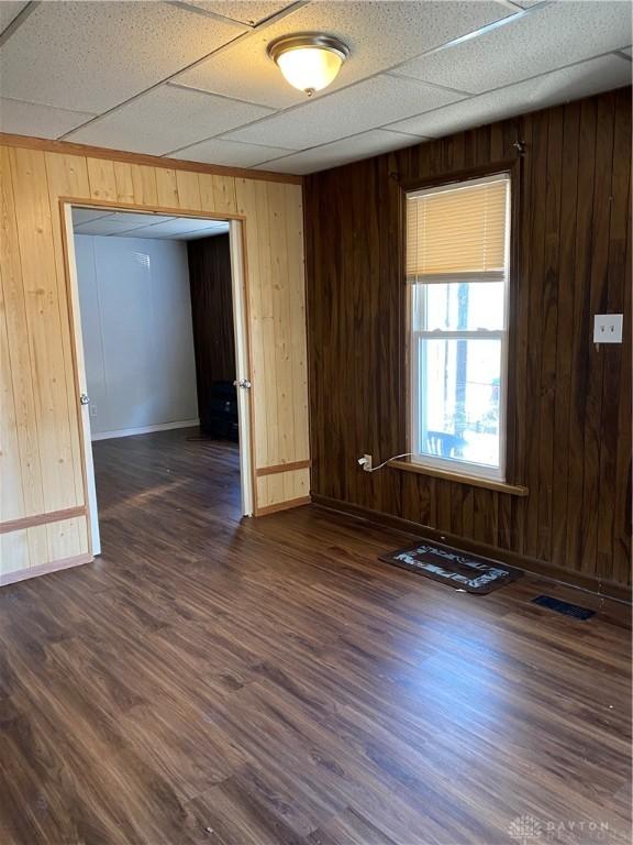 spare room with a paneled ceiling, dark hardwood / wood-style flooring, and wooden walls