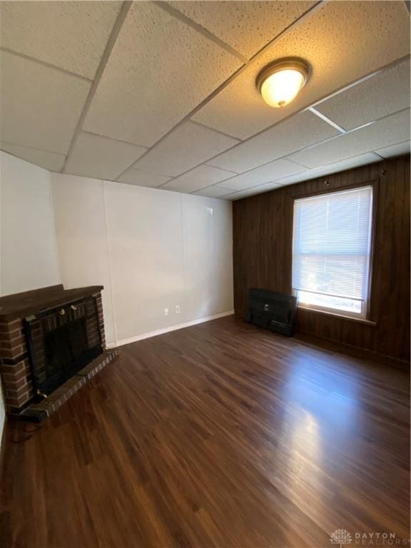 unfurnished living room with a paneled ceiling, dark hardwood / wood-style floors, wood walls, and a fireplace