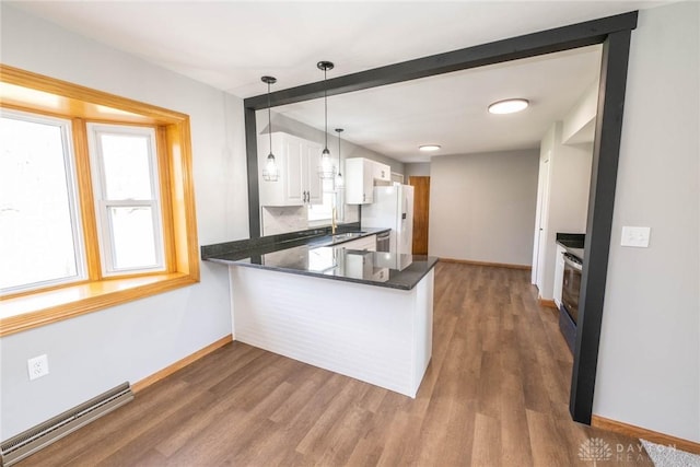 kitchen with white cabinetry, white refrigerator, a baseboard radiator, kitchen peninsula, and pendant lighting