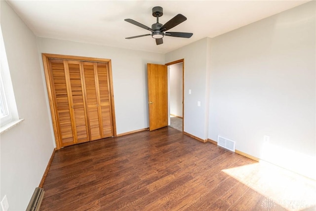 unfurnished bedroom with dark hardwood / wood-style flooring, a closet, ceiling fan, and baseboard heating