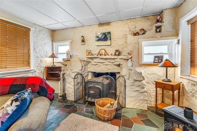 sitting room featuring a wood stove, a drop ceiling, and a healthy amount of sunlight