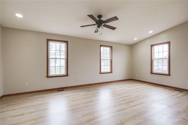 empty room featuring light hardwood / wood-style floors, vaulted ceiling, a wealth of natural light, and ceiling fan