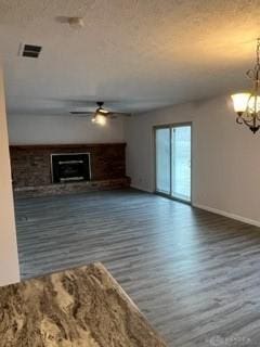 unfurnished living room with a fireplace, dark wood-type flooring, and ceiling fan with notable chandelier