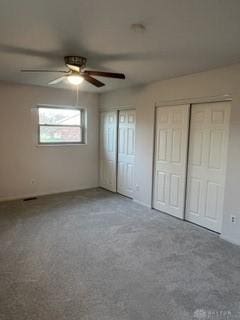 unfurnished bedroom featuring ceiling fan, carpet floors, and two closets