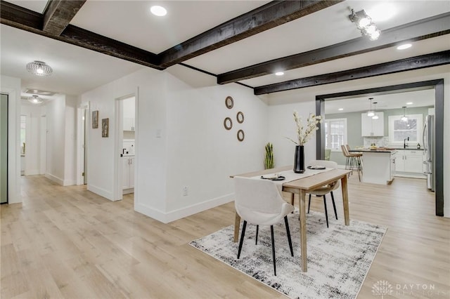 dining area featuring sink, beam ceiling, and light hardwood / wood-style floors