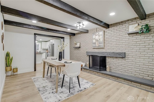 dining space featuring beam ceiling, a fireplace, light hardwood / wood-style floors, and brick wall