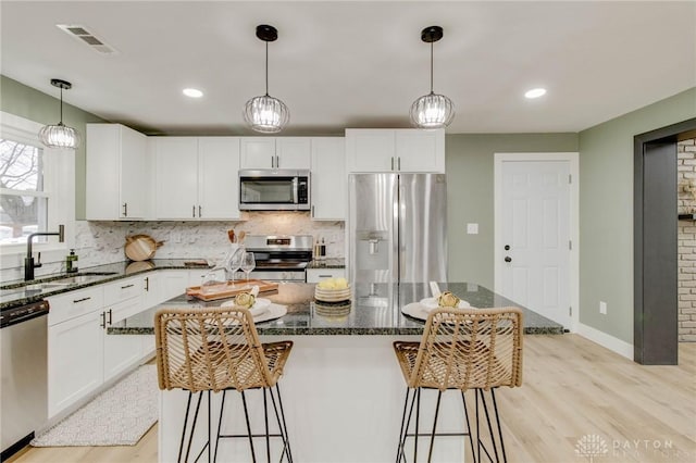 kitchen featuring a kitchen island, appliances with stainless steel finishes, sink, white cabinets, and hanging light fixtures