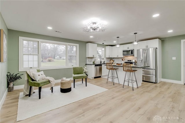 kitchen with a breakfast bar, appliances with stainless steel finishes, white cabinetry, backsplash, and a center island