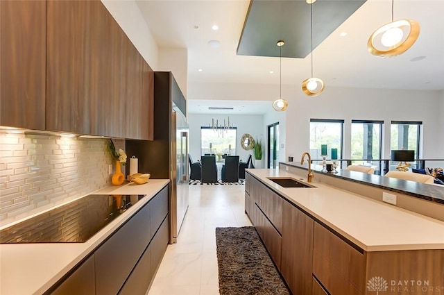 kitchen with black electric stovetop, sink, hanging light fixtures, and tasteful backsplash