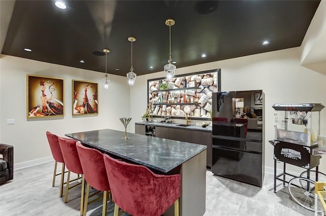 kitchen with a center island, sink, hanging light fixtures, dark stone countertops, and a breakfast bar area