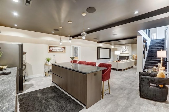 kitchen with pendant lighting, dark stone counters, a kitchen island, dark brown cabinetry, and stainless steel refrigerator