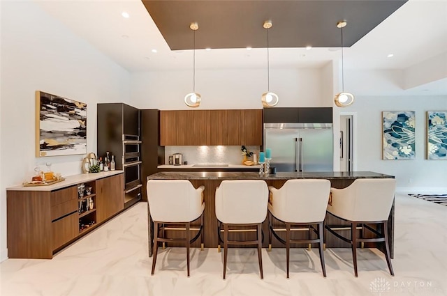 kitchen featuring a kitchen island with sink, decorative backsplash, a towering ceiling, decorative light fixtures, and stainless steel appliances