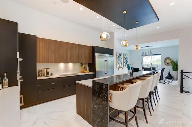 kitchen with tasteful backsplash, decorative light fixtures, a center island with sink, a breakfast bar area, and built in fridge