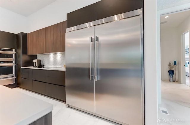 kitchen with dark brown cabinets, stainless steel appliances, and tasteful backsplash