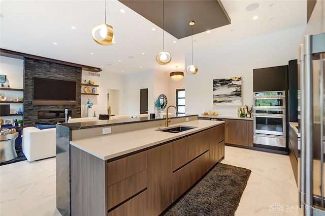 kitchen featuring a large fireplace, double oven, a spacious island, sink, and hanging light fixtures