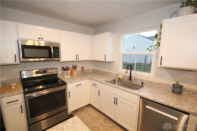 kitchen featuring light stone counters, stainless steel appliances, white cabinetry, and sink