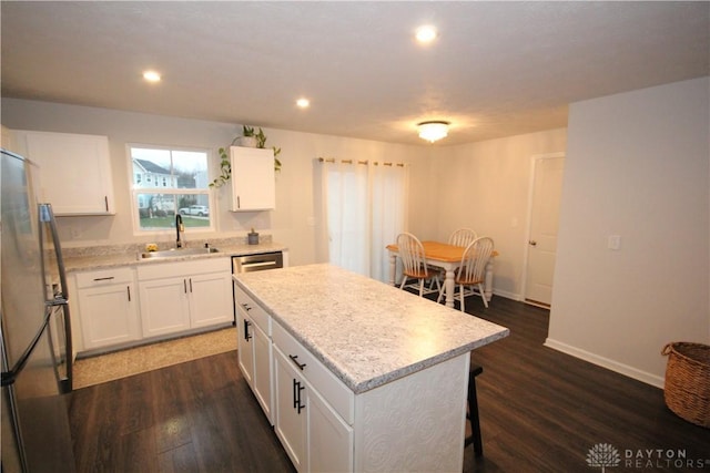 kitchen with sink, a kitchen island, dark hardwood / wood-style flooring, white cabinetry, and stainless steel refrigerator