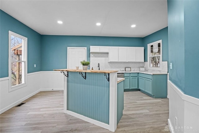 kitchen featuring a breakfast bar area, backsplash, white cabinets, and light hardwood / wood-style floors