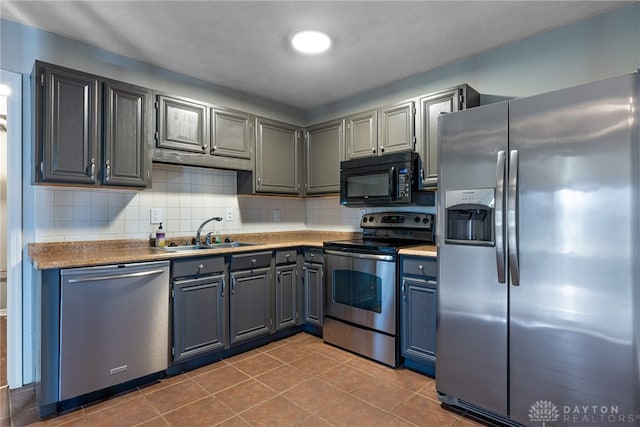 kitchen featuring sink, tile patterned flooring, gray cabinets, decorative backsplash, and appliances with stainless steel finishes