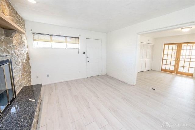 unfurnished living room featuring a fireplace, french doors, and light wood-type flooring