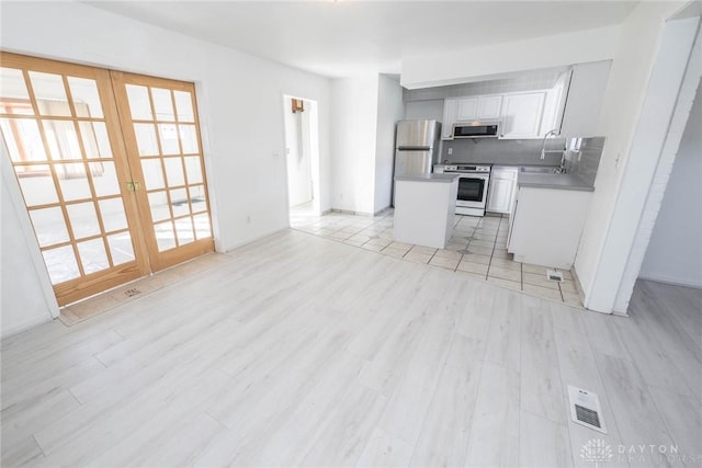 kitchen featuring decorative backsplash, french doors, stainless steel appliances, white cabinets, and a center island