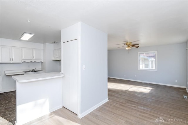 kitchen featuring light wood finished floors, ceiling fan, light countertops, white cabinetry, and a sink