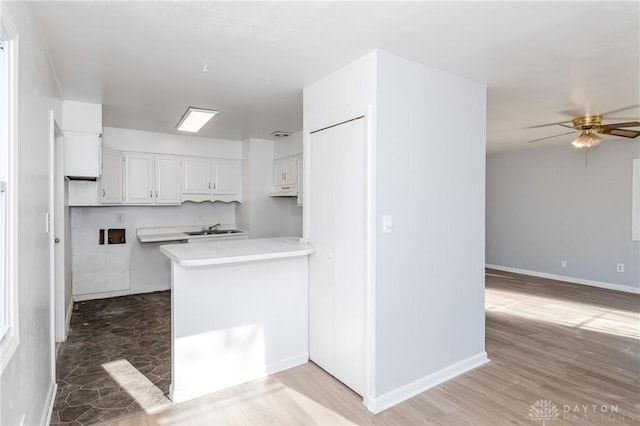 kitchen with a peninsula, ceiling fan, a sink, light countertops, and white cabinets